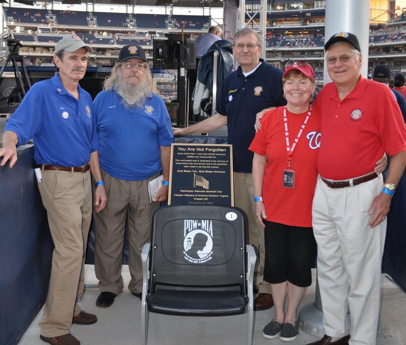 Five Chapter 227 members standing on either side of a black POW/MIA chair and its bronze dedication plaque in the stands at Nationals Park.